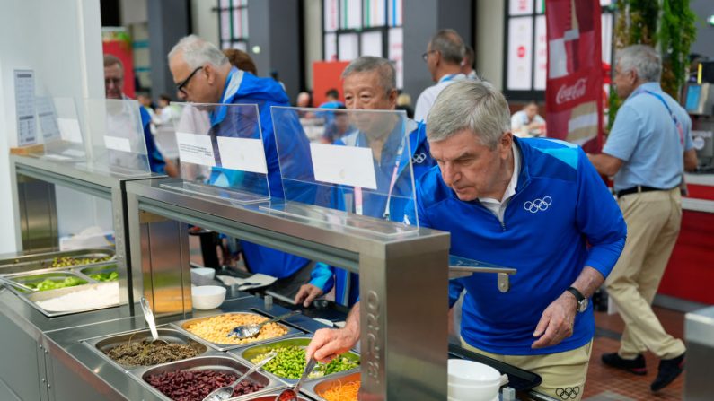 Le président allemand du Comité international olympique (CIO) Thomas Bach goûte à la nourriture d'un bar à salades lors d'une visite au village olympique, à Saint-Denis, le 22 juillet 2024. (Photo :  DAVID GOLDMAN/POOL/AFP via Getty Images)