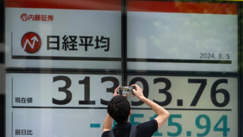 Un passant prend une photo des écrans affichant l'indice Nikkei 225 Stock Average à l'extérieur d'une société d'investissement de Tokyo, au Japon, le 5 août 2024. (Tomohiro Ohsumi/Getty Images)