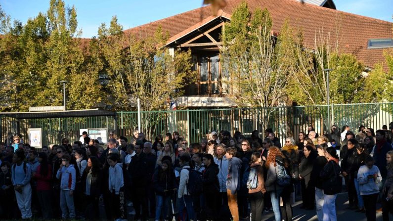 Des personnes observent une minute de silence lors d'une cérémonie d'hommage aux enseignants français Samuel Paty et Dominique Bernard devant le collège du Bois d'Aulne à Conflans-Sainte-Honorine, dans les Yvelines, le 16 octobre 2023. (Photo : BERTRAND GUAY/AFP via Getty Images)