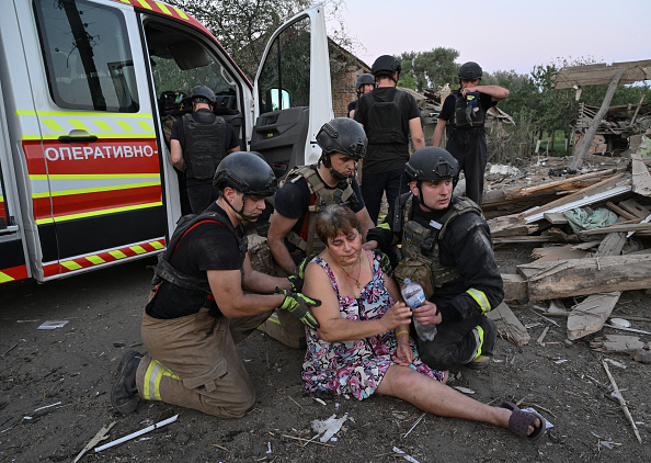 Des sauveteurs aident une femme qui s'est évanouie devant la maison détruite à Sumy, le 18 août 2024, dans le contexte de l'invasion russe de l'Ukraine. (GENYA SAVILOV/AFP via Getty Images)