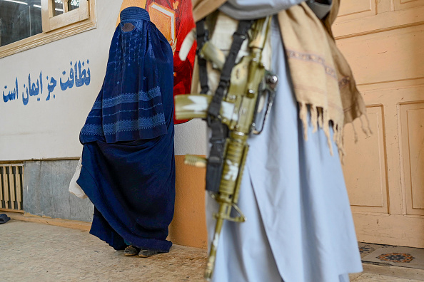 Le personnel de sécurité taliban monte la garde alors qu'une femme afghane vêtue d'une burqa attend de recevoir un kit d'hiver de l'UNICEF à Fayzabad, en février 2024. (WAKIL KOHSAR/AFP via Getty Images)