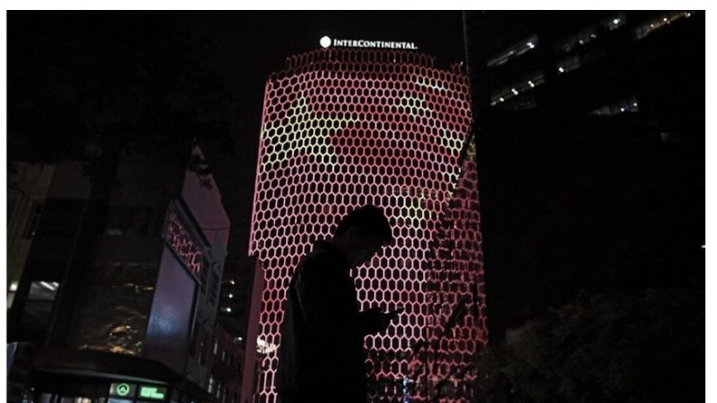 Un homme regarde son téléphone près d'une image géante du drapeau national chinois projetée sur la façade d’un immeuble à Pékin, lors du 19e Congrès du Parti communiste chinois, le 23 octobre 2017. (Greg Baker/AFP via Getty Images)