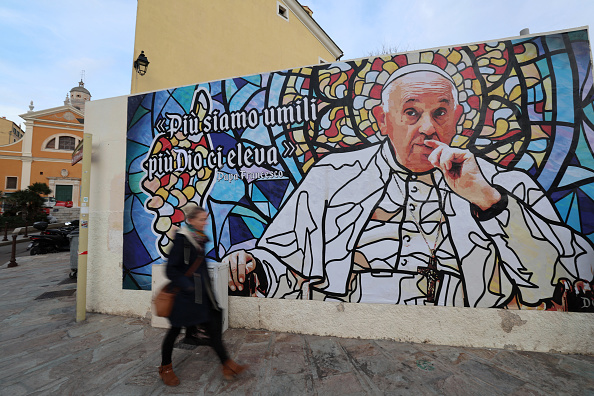 Une femme marche devant une fresque représentant le pape François près de la cathédrale d'Ajaccio, à Ajaccio en Corse, le 10 décembre 2024. (PASCAL POCHARD-CASABIANCA/AFP via Getty Images)