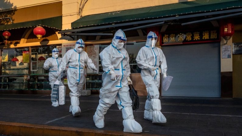 Des agents de lutte contre la propagation du Covid-19 passent devant un magasin fermé près d'une communauté dont les habitants font l'objet d'une surveillance sanitaire, à Pékin, le 4 décembre 2022. (Kevin Frayer/Getty Images)